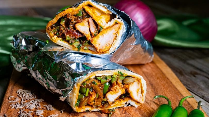 Two chicken wraps, cut in half, revealing chicken, peppers, and onions, on a wooden board.