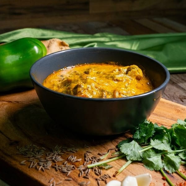 A bowl of yellow curry with green peppers, cilantro, and spices on a wooden board.