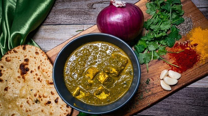 Palak Paneer with naan bread, red onion, cilantro, garlic, and spices on a wooden board.